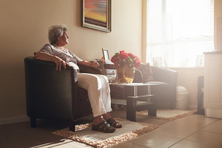 Senior vrouw zit op de bank en kijkt naar buiten