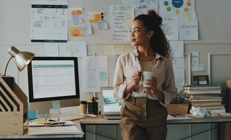 Persoon staat aan bureau met computer en papieren