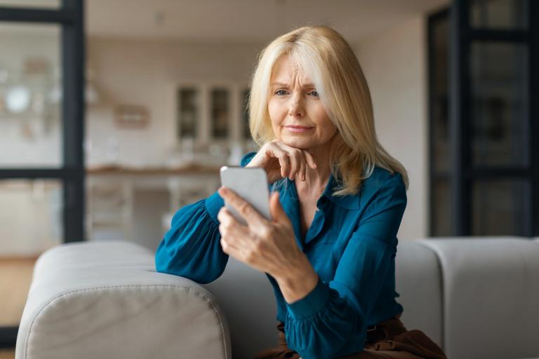 Vrouw in huiskamer kijkt bezorgd op mobiele telefoon