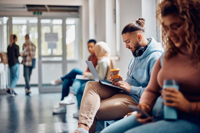 Studenten zitten in gang van hogeschool of universiteit met laptops en smartphones