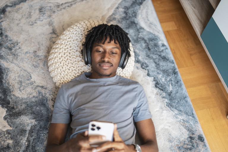 Man met telefoon en koptelefoon ligt op tapijt in woonkamer